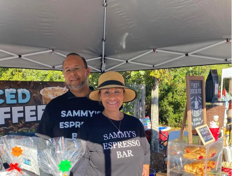 Sammy and Tania at their espresso stand, with an iced coffee banner and treats on the table